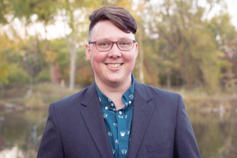 A white person with short brown hair and glasses, wearing a suit jacket outdoors